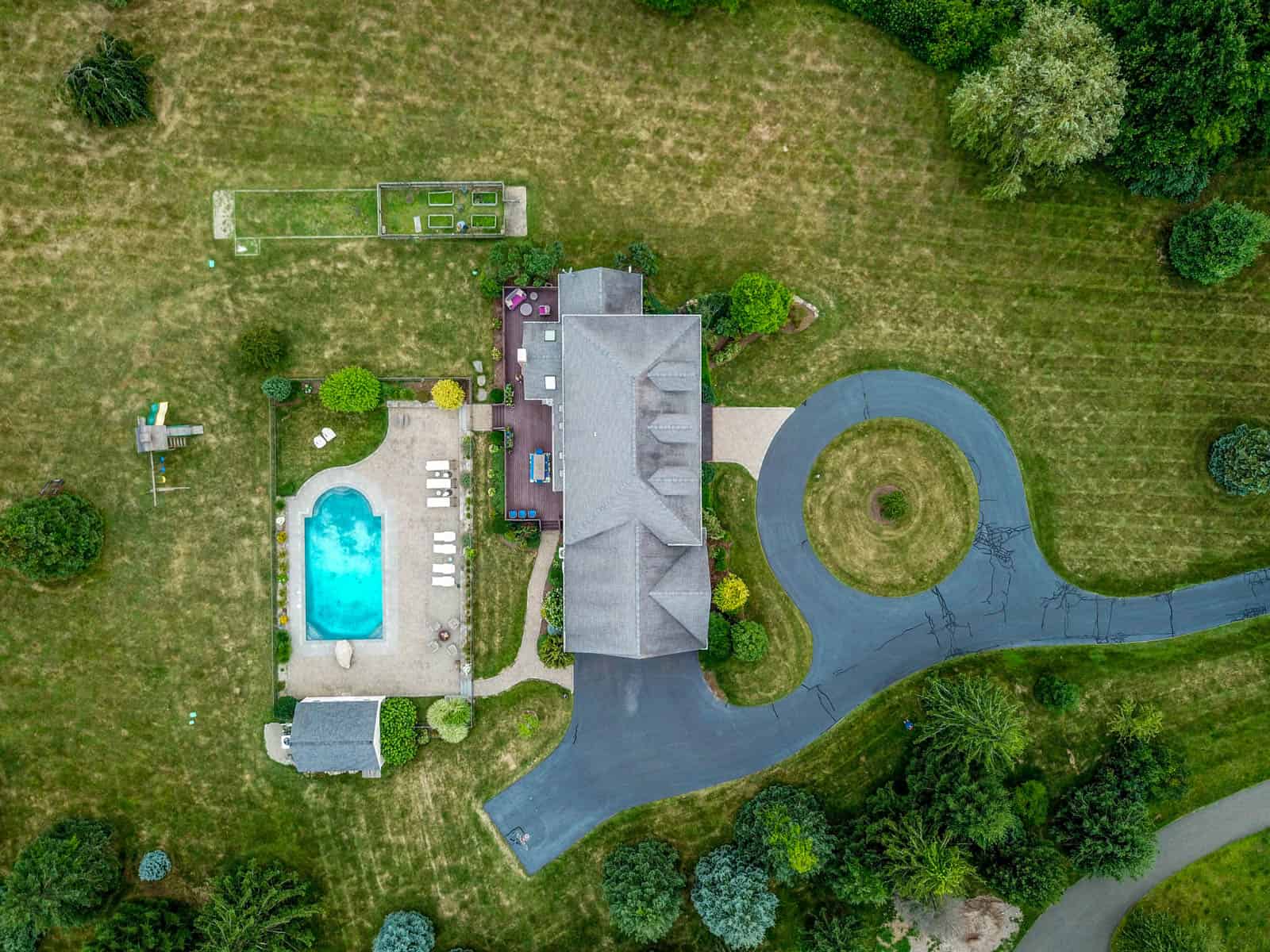 looking down at Connecticut home with mown lawn, circular driveway, and swimming pool in backyard with fire pit