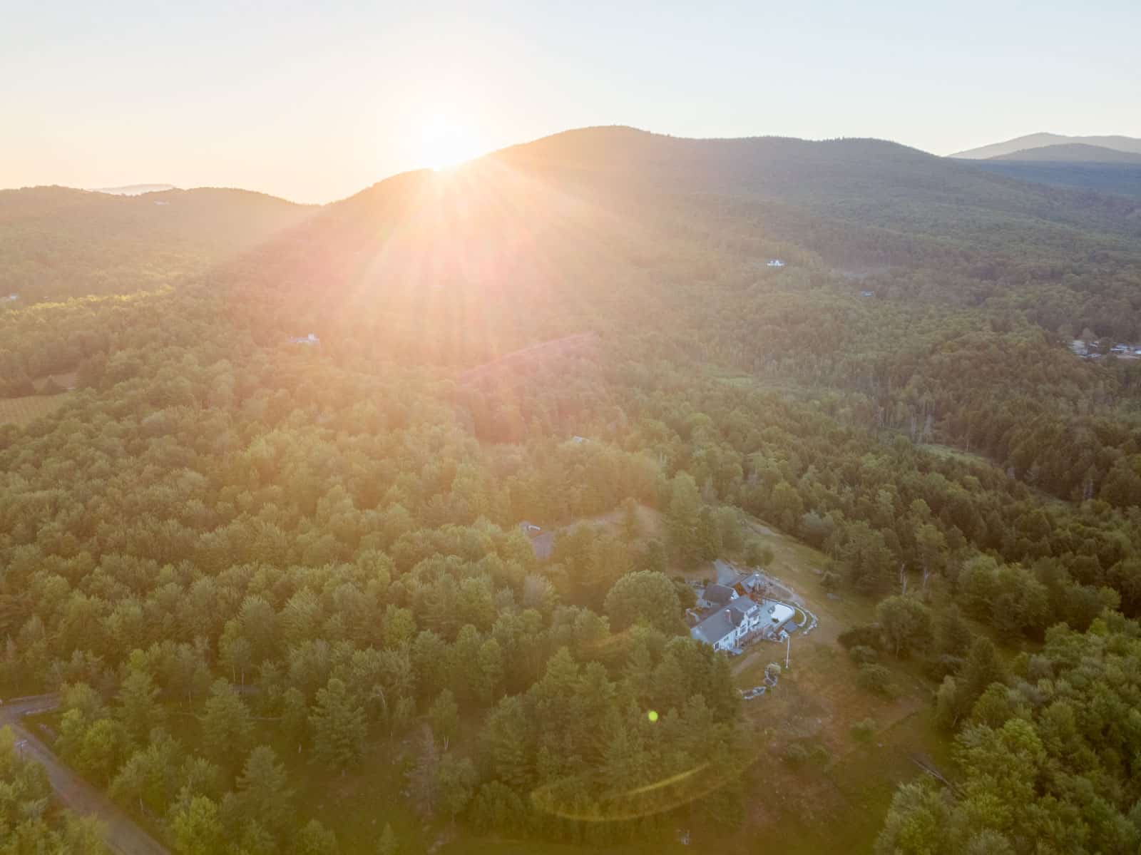 drone photo of house in Vermont with sun peaking up over mountain in background