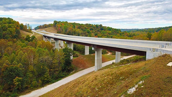 photo of bridge going diagonally through hilly landscape with conifer trees